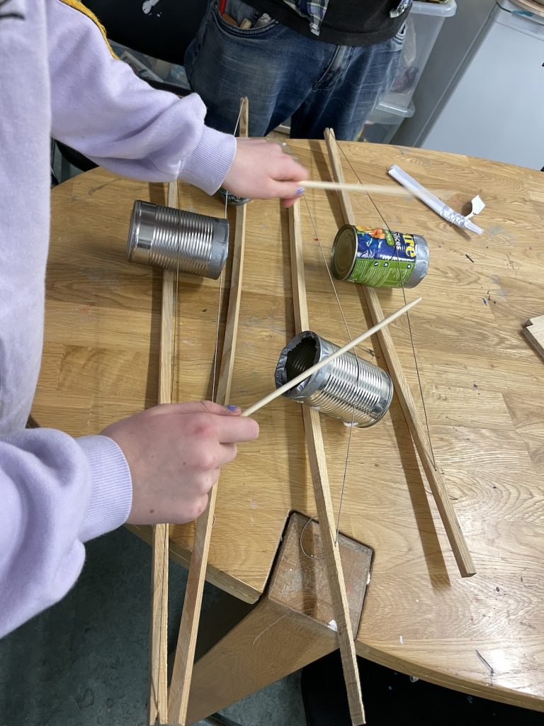 A childs hands with chopsticks tapping a tin can and wooden nstreument