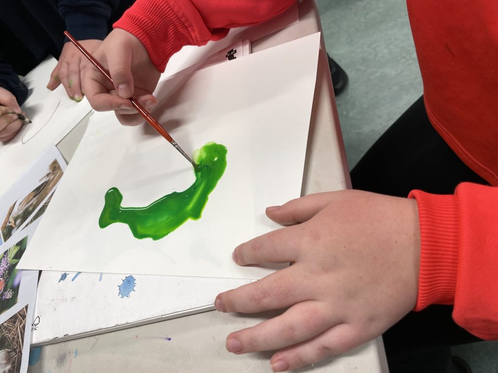 a child's hands making an inky green shape on paper