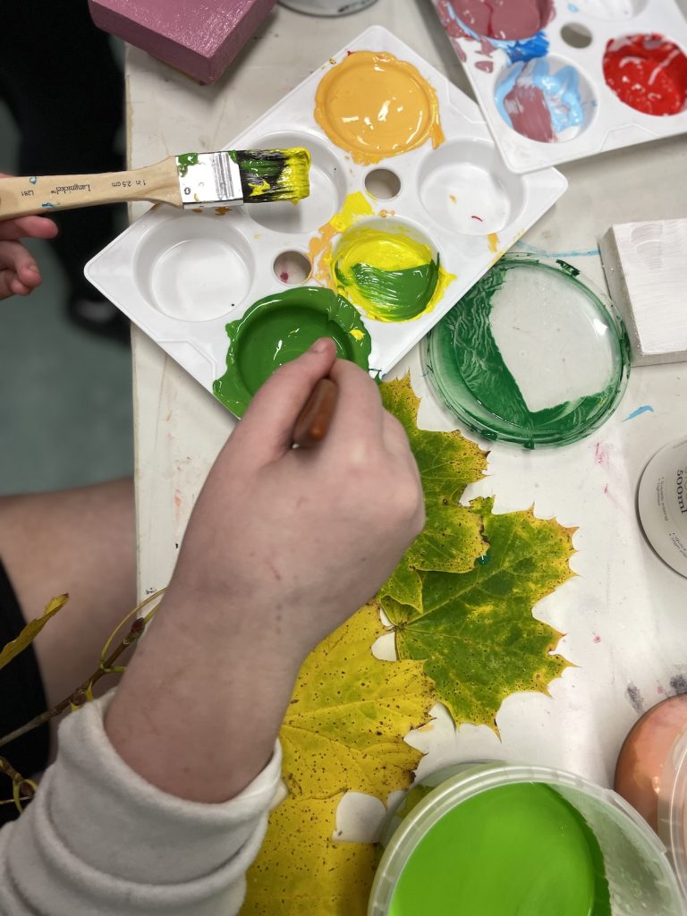 photo of a hand and a loaded paint brush with leaves