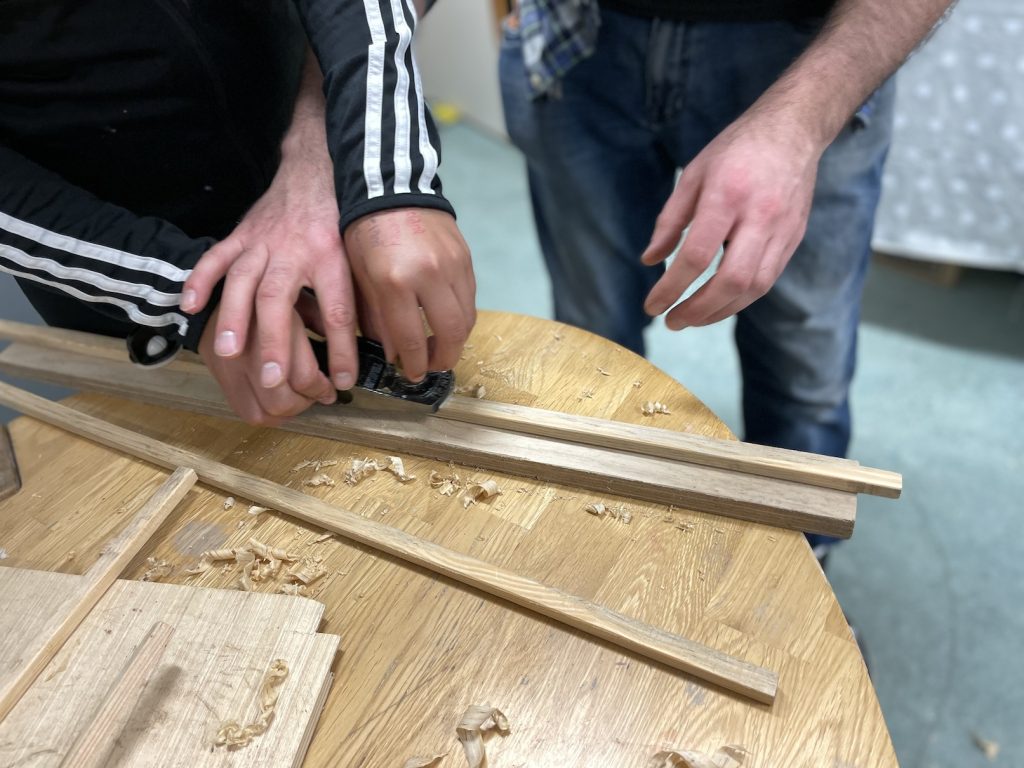 A photo of child and an adult's hands moving a plane across a timber strip