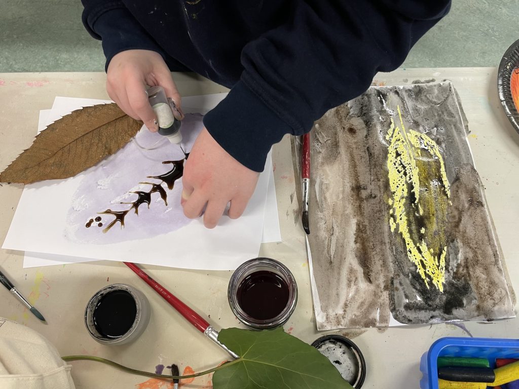 A child making inky wax release paitnings with leaves 