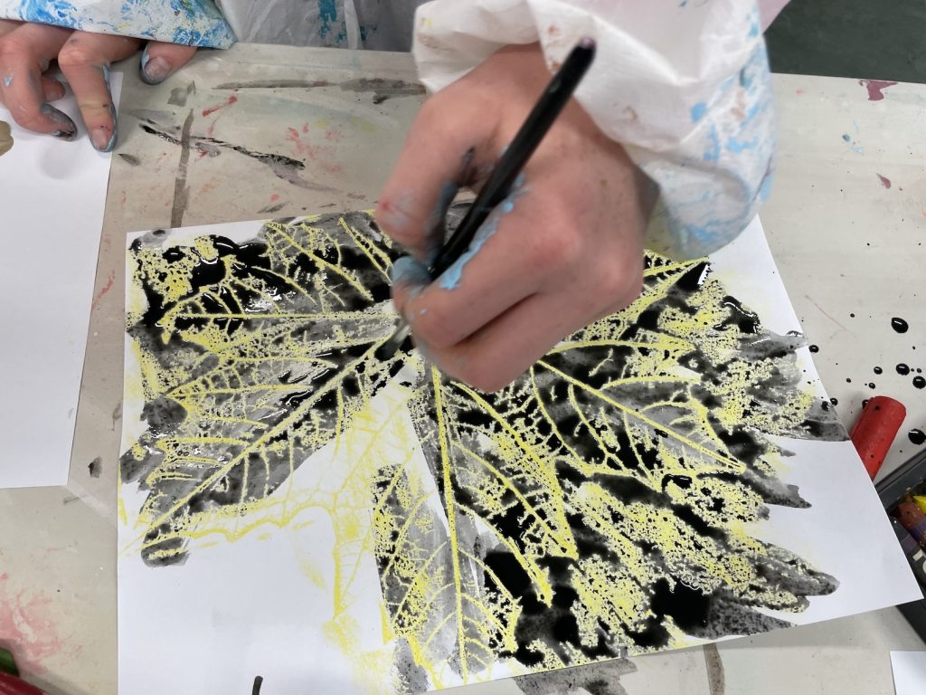 a photo of a child making a leaf drawing with ink and wax relief