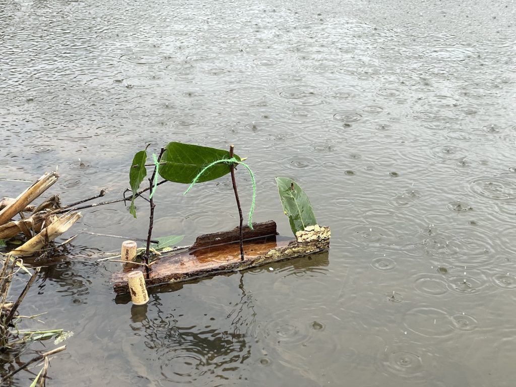 A photo of a toy boat made from bark and corks floating on water in the rain