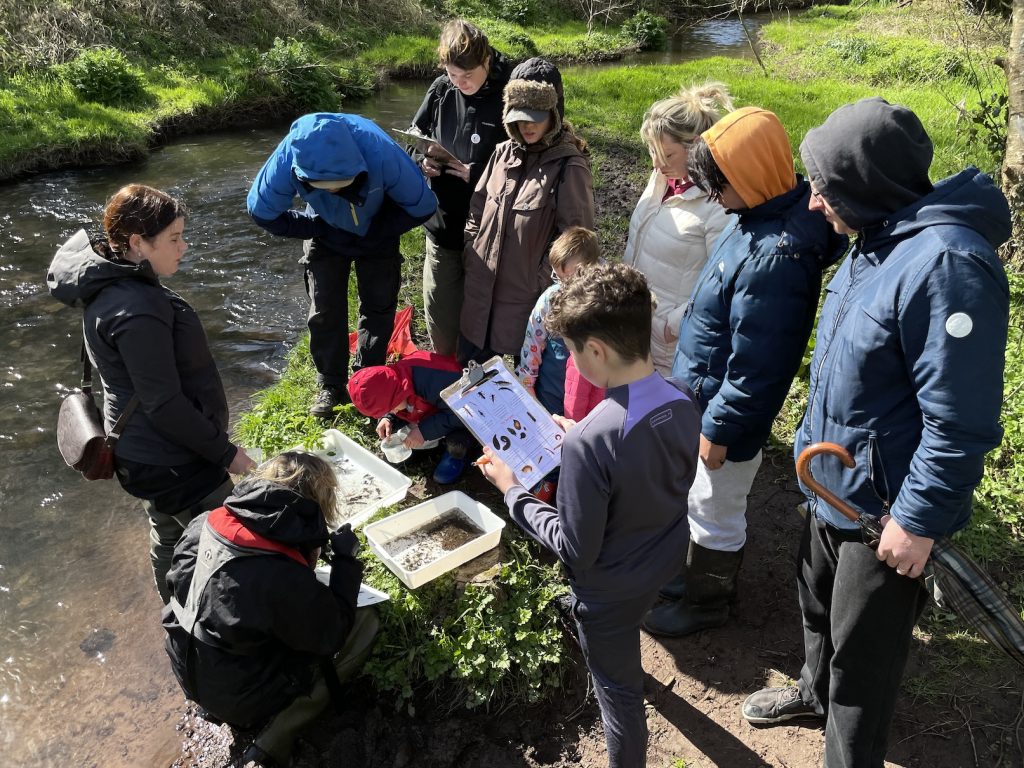 a photo of a group of people on a river bank looking into a white basin and holding record sheets