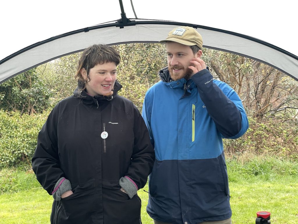 A photograph of a woman and a man under a gazebo in a green space these are Annie Mar and Aaron Ross also known as Spoon and Bloom in the Glen