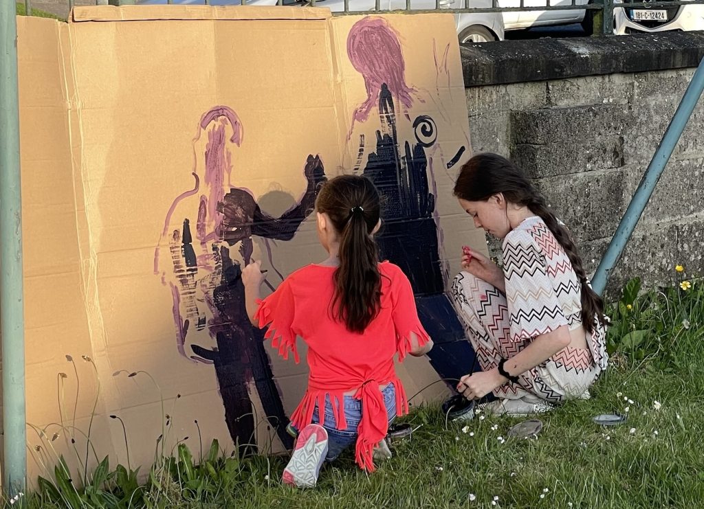 A photo of two girls painting silhoettes onto cardboard