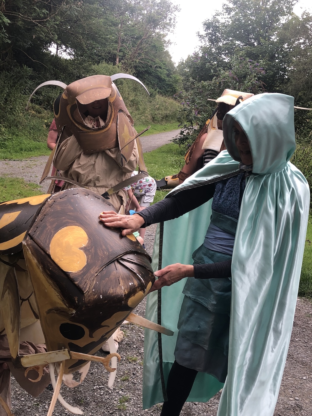 A photo of a woman dressed as the river guardian touching the head of a man in a costume of a stonefly nymph