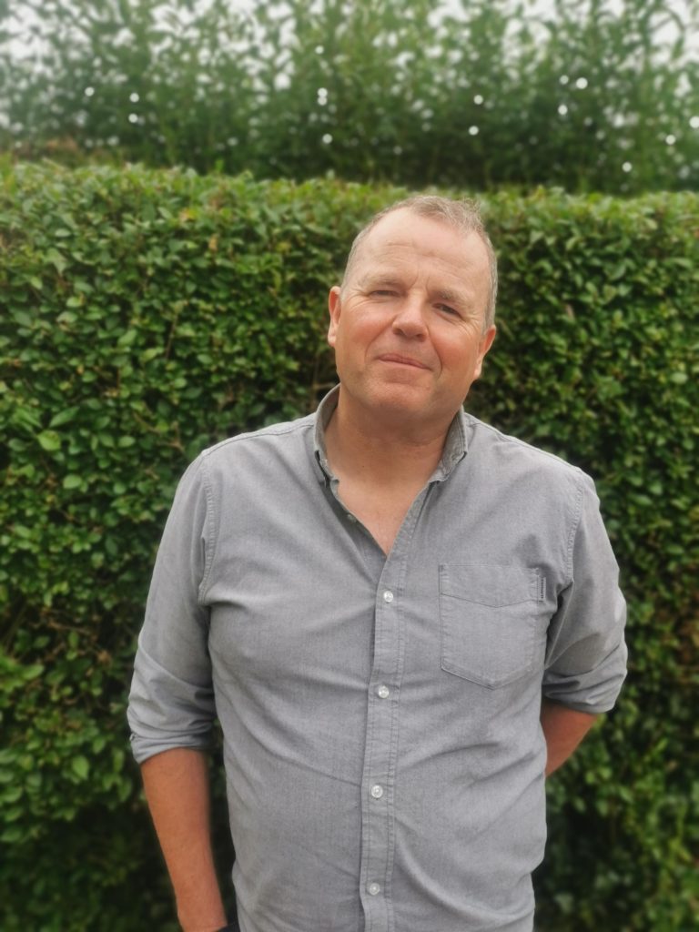 a photo of a man standing in fron of a hedge