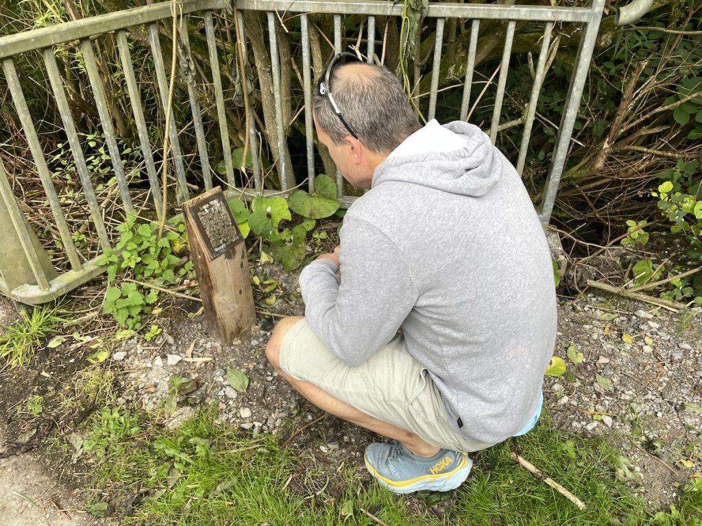 A man crousching down in front of a plaque for the FauimMná trail with a QR Code on it