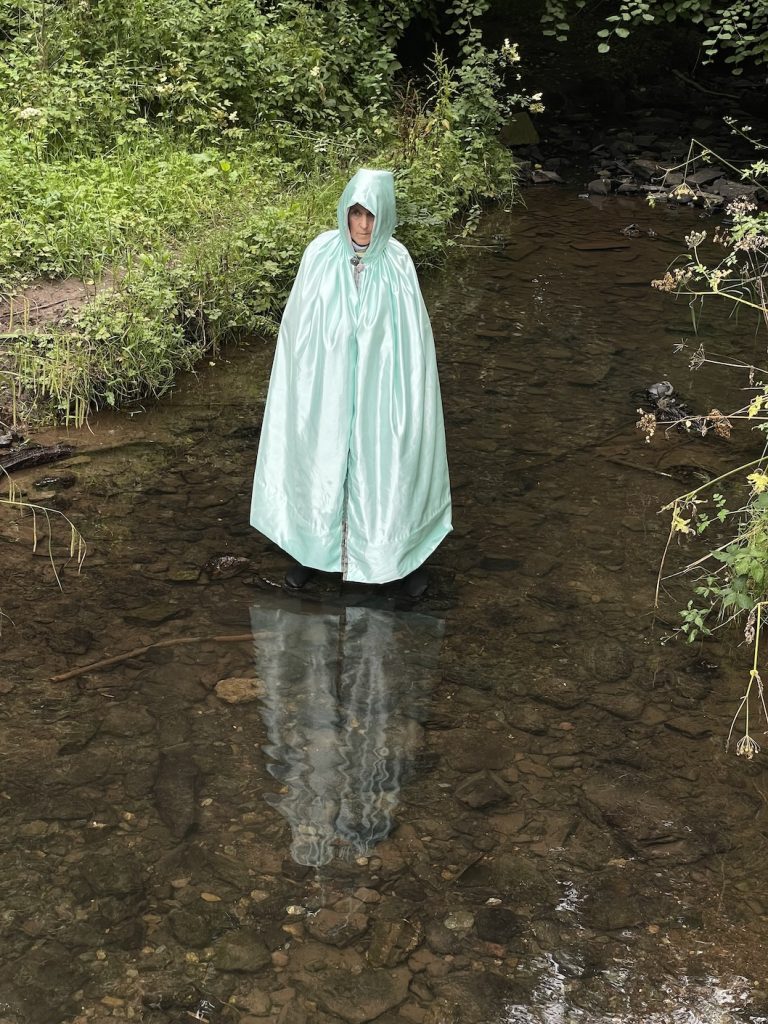 a woman in a siver-green cape standing in the river