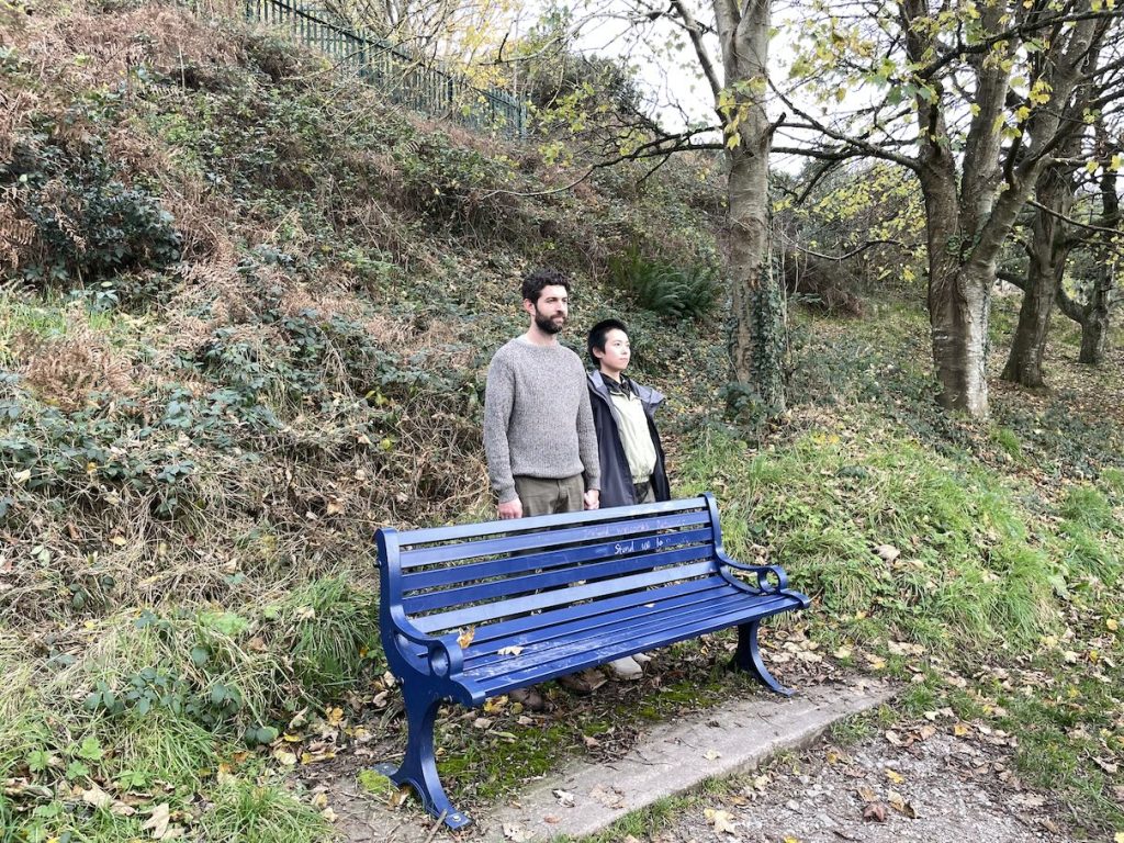 A man and a woman standing behind a bench in a park