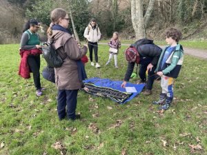 a photo of people gathering around a cloth on the ground with divining rods, pendulums and hazels on it