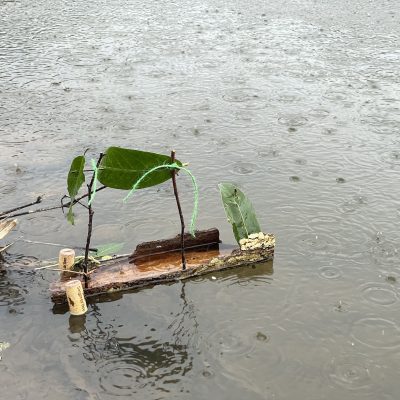 A photo of a toy boat made from bark and corks floating on water in the rain