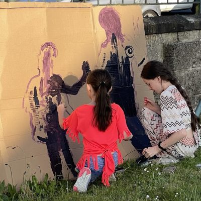 A photo of two girls painting silhoettes onto cardboard