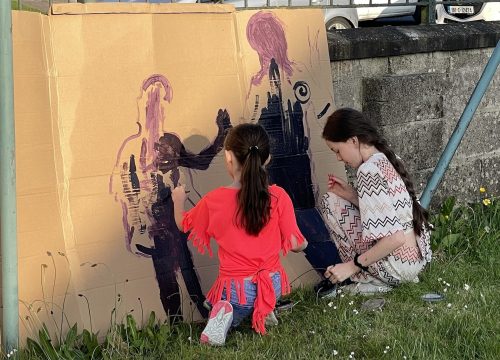 A photo of two girls painting silhoettes onto cardboard