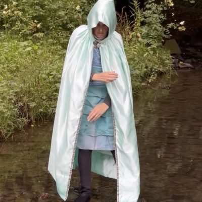 a photo of a woman in a pale blue claok standing in the river