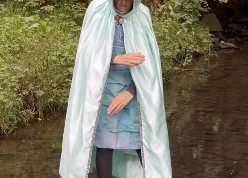 a photo of a woman in a pale blue claok standing in the river