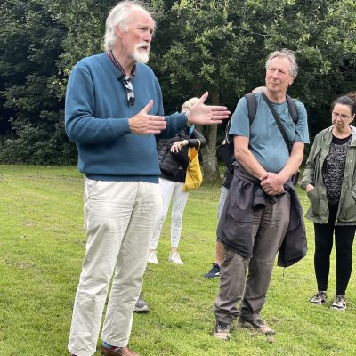 a photograph of a man with white hair and a beard talking to an audeince in the park