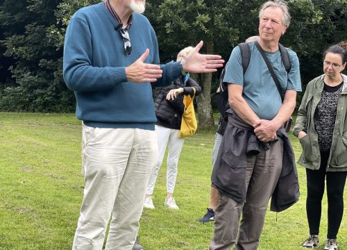 a photograph of a man with white hair and a beard talking to an audeince in the park